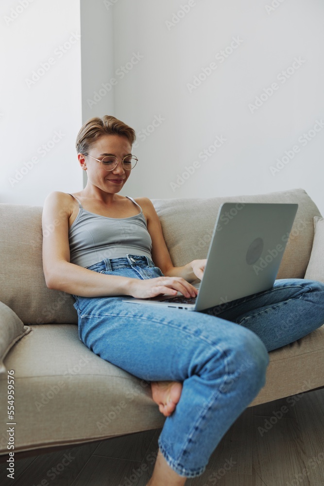 Teenage girl freelancer with laptop sitting on couch at home smiling in home clothes and glasses with short haircut, lifestyle with no filters, free copy space Teenage girl freelancer with laptop sitting on couch at home smiling in home clothes and glasses with short haircut, lifestyle with no filters, free copy space