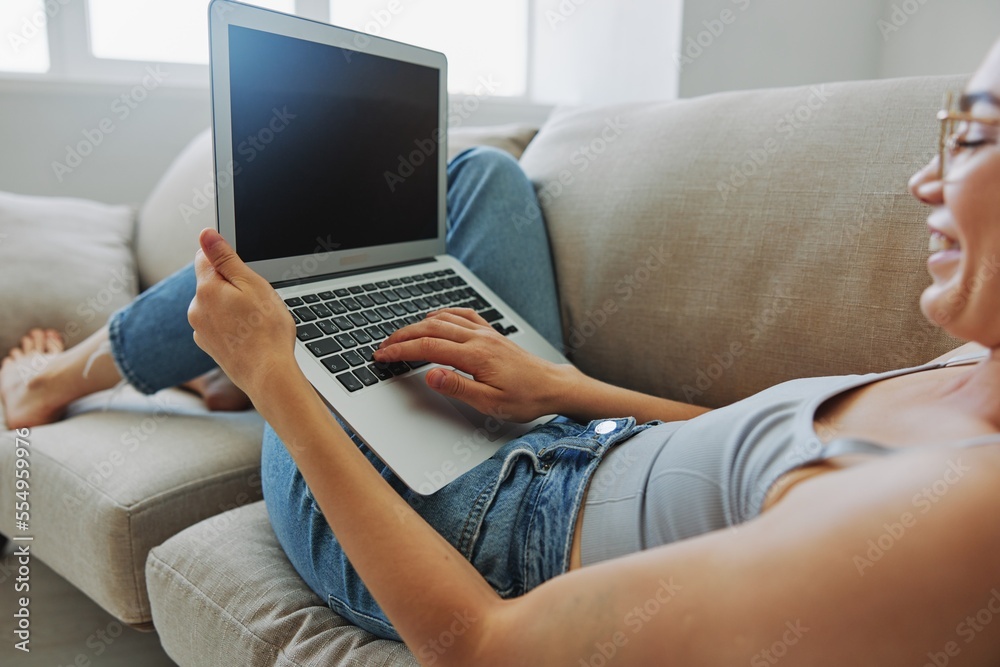 Fototapeta premium Teenage girl freelancer with laptop sitting on couch at home smiling in home clothes and glasses with short haircut, lifestyle with no filters, free copy space