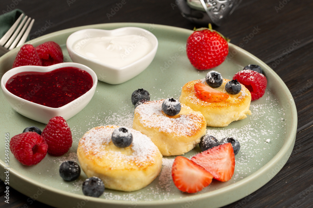 Cheesecakes are laid out in the shape of a Snowman, decorated with berries, sprinkled with powdered sugar, with toppings of berry jam and sour cream Cheesecakes are laid out in the shape of a Snowman, decorated with berries, sprinkled with powdered sugar, with toppings of berry jam and sour cream