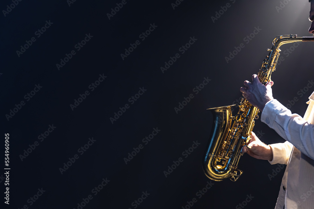 Fototapeta premium Saxophone in the hands of a man on a dark background, copy space.