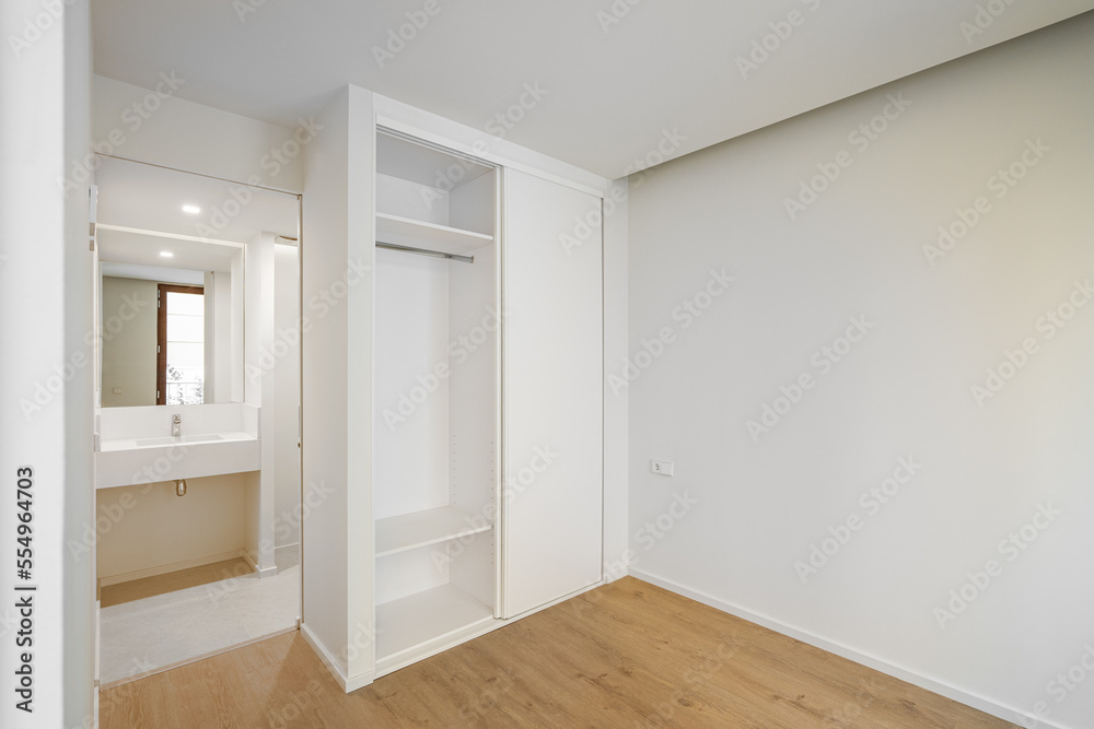 Bright spacious bedroom with parquet flooring with a built-in wardrobe for clothes and linen. An open door from the room leading to a bathroom with a washbasin and a small mirror. Bright spacious bedroom with parquet flooring with a built-in wardrobe for clothes and linen. An open door from the room leading to a bathroom with a washbasin and a small mirror.