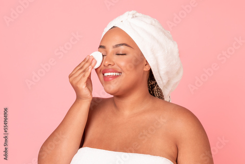 Fotografia Attractive black plus size woman touching her face with cotton pad, removing mak