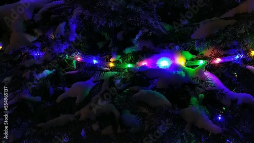 colored and Christmas garlands glow with bright colors and on the Christmas tree at night in the park