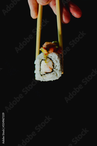 Sushi roll held by chopsticks on black background