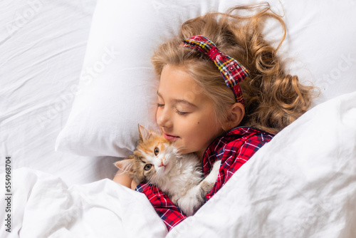 a cute little girl is sleeping sweetly at home in a rabbit with a kitten. White cotton bed linen. Christmas holidays. Children and pets at home