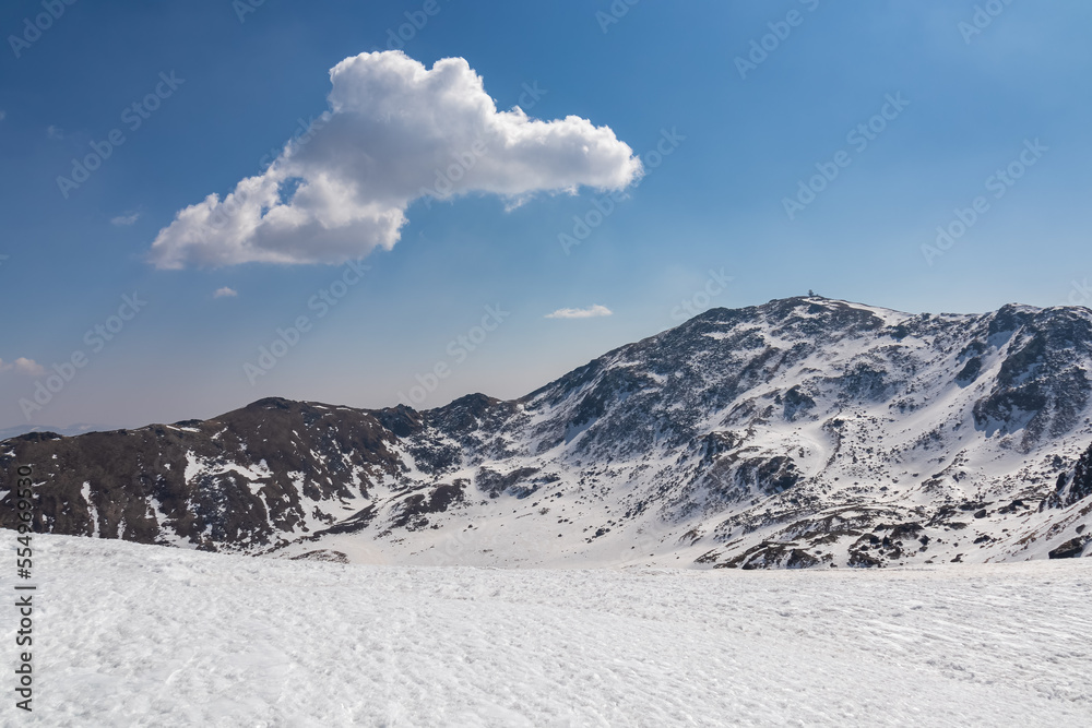 Snow covered alpine pasture with panoramic view on snowcapped mountain ridges of summit Zirbitzkogel in Seetal Alps, Styria, Austria, Europe. One single cloud hiking trail Central Alps in sunny winter