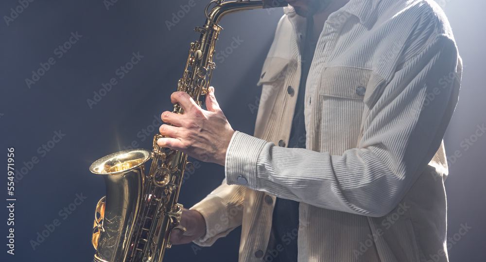 Fototapeta premium Male musician on stage plays the saxophone dark with smoke.