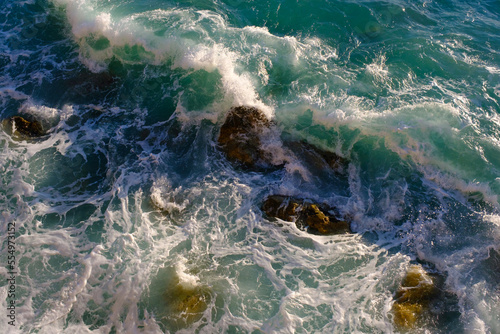 Sea water breaking on rocks, outdoors, waves and stones, splash and foam, top view.