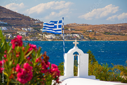 Greek seaside island Mykonos coast landscape with flag and religious church on a sunny and windy day in the Aegean sea