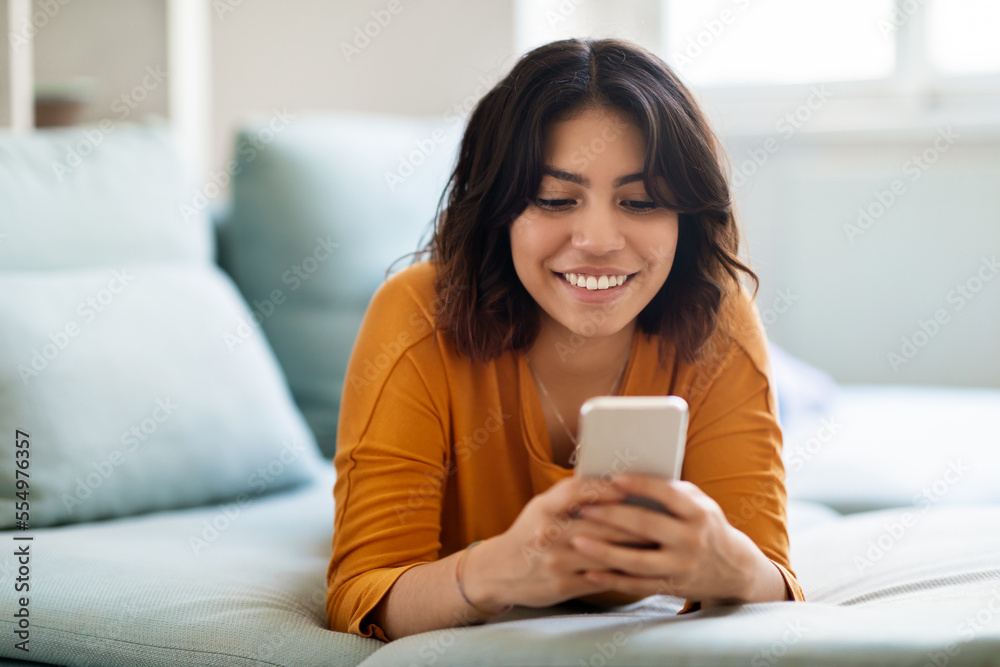 Mobile Communication. Cheerful Arab Female Messaging On Smartphone While Lying On Couch Mobile Communication. Cheerful Arab Female Messaging On Smartphone While Lying On Couch