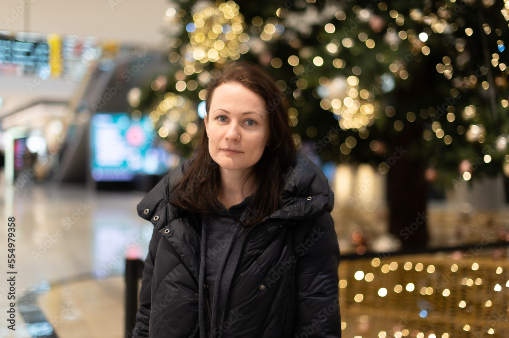 Fototapeta premium Portrait of a beautiful woman on the background of a Christmas tree with bright lights gerlant. Beautiful multicolored bokeh in the background