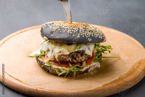 Black Burger with meat, aragula and vegetables on the board on grey table photo