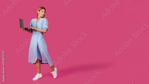 Happy adult caucasian blonde female in dress with laptop looks at empty space for ad and offer