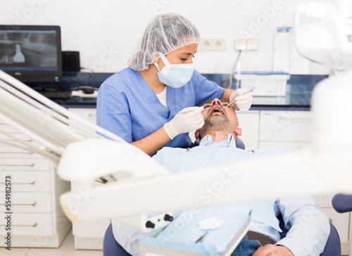 Professional dentist woman inspects patient teeth with dental tools - mirror and probe