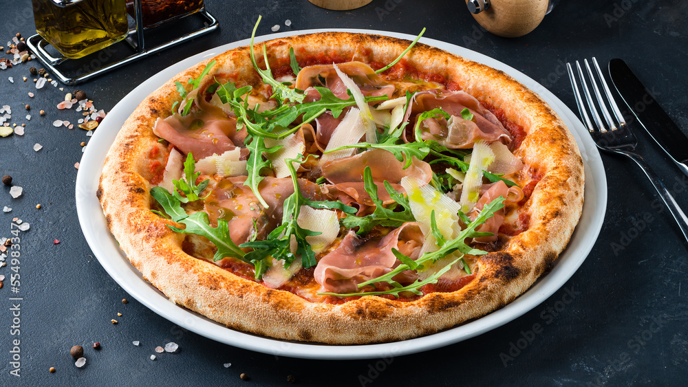 Italian cuisine pizza with ham, parmesan, tomato sauce, arugula and spices. Italian cuisine pizza with ham, parmesan, tomato sauce, arugula and spices.