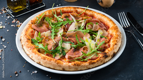 Italian cuisine pizza with ham, parmesan, tomato sauce, arugula and spices.