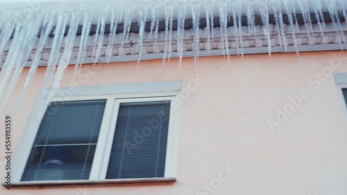 Large icicles hang from the overhang of the roof of the building. Falling ice- winter hazard for passersby