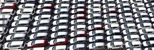 Aerial view of new cars stock at factory parking lot. Above view many cars parked in a row. Automotive industry. Logistics and supply chain business. Import or export new cars at warehouse near port.