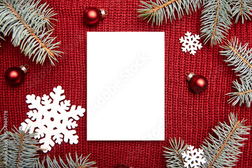 Christmas greeting card mockup, fir tree branches and holiday decorations on red knitted sweater background, top view, flat lay. Blank New Year card with winter decor, wooden snowflakes and balls