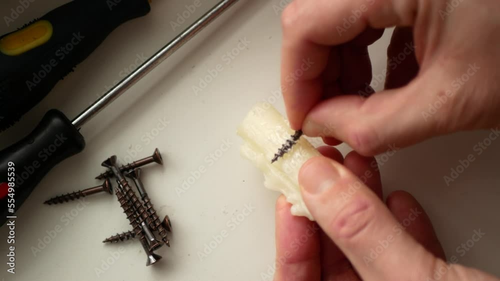 Woodworker is rubbing some candle wax on the screws before driving them into wood joints. Wax coating screws, selective focus. Concept of crafty idea or life hack