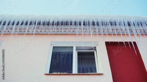 Large icicles hang from the overhang of the roof of the building. Falling ice- winter hazard for passersby photo