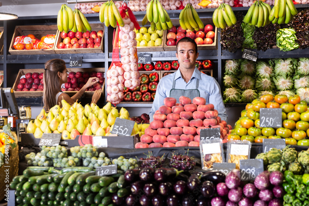 Posing glad male and working woman in fruit and vegetable shop