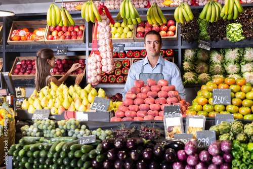 Posing glad male and working woman in fruit and vegetable shop