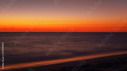 Vibrant orange red sky reflecting in calm ocean after sunset. Minimal landscape photo with space for text