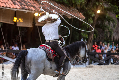 Horseman also known as Mexican charro in a magnificent exhibition of movements with the sliding lasso on a spectacular Aztec horse that handles the lasso in an incredible way at Xcaret Park in Mexico. photo