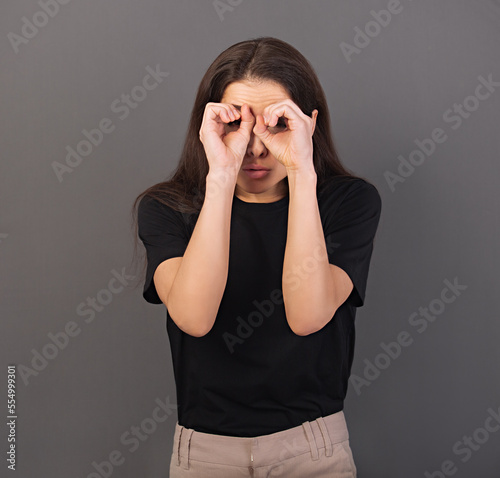 Happy excited woman doing spyglass sign looking in by fingers the hands with surprising opened mouth in black t-shirt. Concept