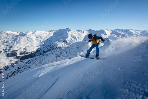 Side view of active freerider snowboarder jumping down snow-covered slope against backdrop of beautiful winter mountain landscape