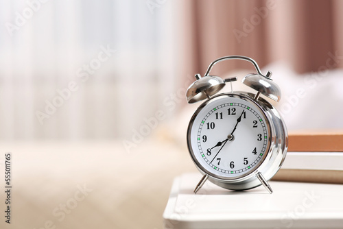 Silver alarm clock on white nightstand indoors. Space for text