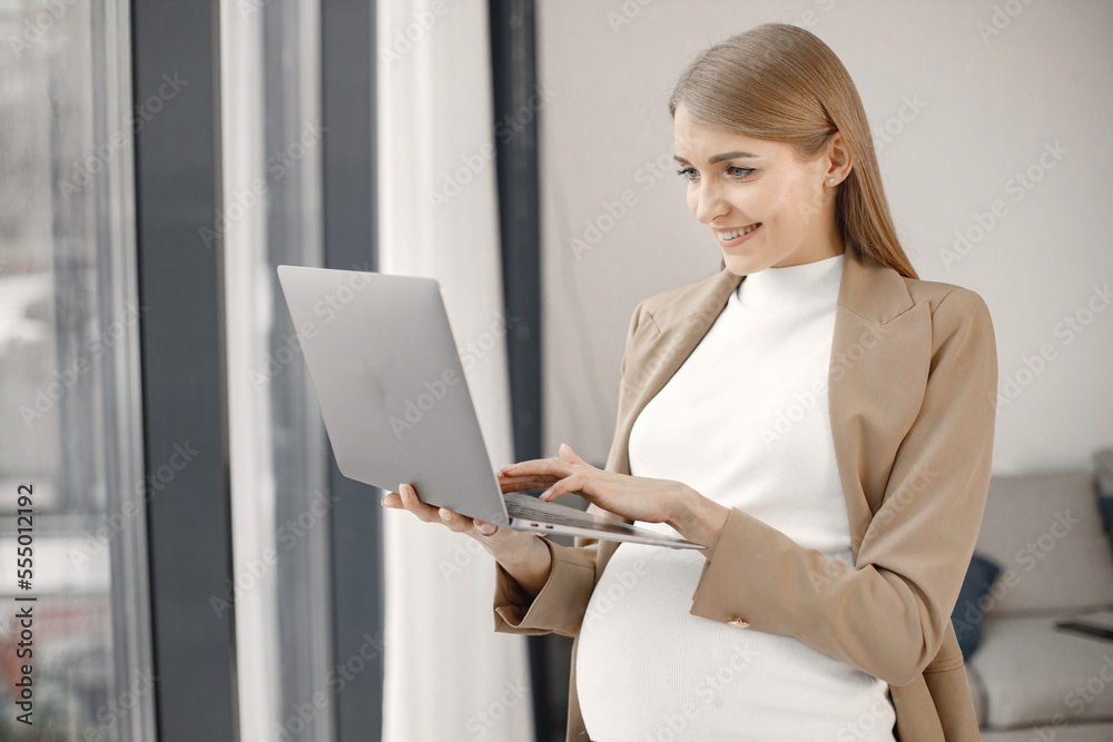 Pregnant lady typing on a laptop while standing in modern office Pregnant lady typing on a laptop while standing in modern office