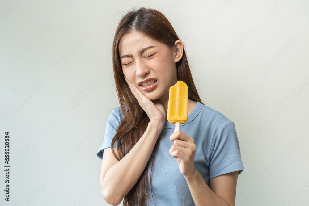 Face expression suffering from sensitive teeth and cold, asian young woman, girl feeling hurt, pain eating ice cream, lolly. Toothache molar tooth at home, dental problem isolated on white background. Face expression suffering from sensitive teeth and cold, asian young woman, girl feeling hurt, pain eating ice cream, lolly. Toothache molar tooth at home, dental problem isolated on white background.