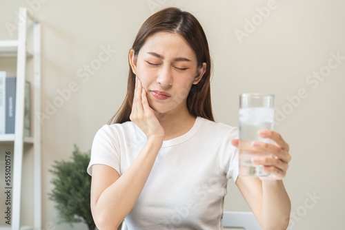 Suffering from toothache, asian young woman, girl touch cheek, face expression ache or feel pain, sensitive molar teeth, hand holding glass of water with ice, inflammation when drink cold, healthcare.