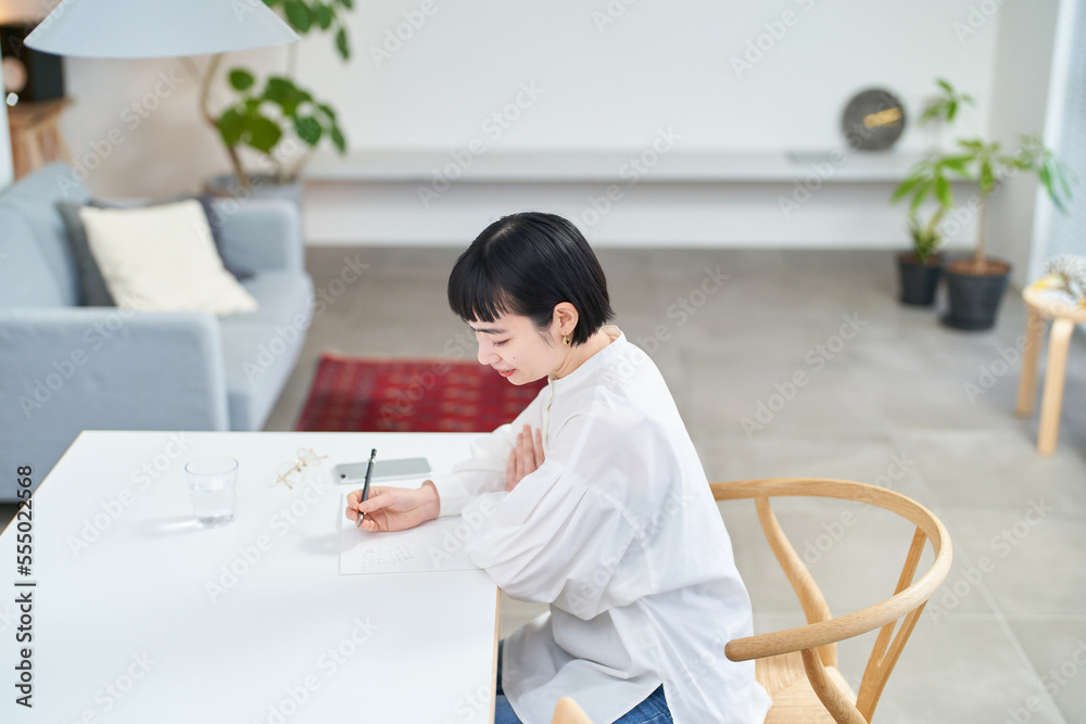 部屋でノートに書きものをする若い女性 部屋でノートに書きものをする若い女性