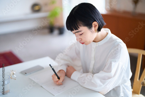 部屋でノートに書きものをする若い女性 photo