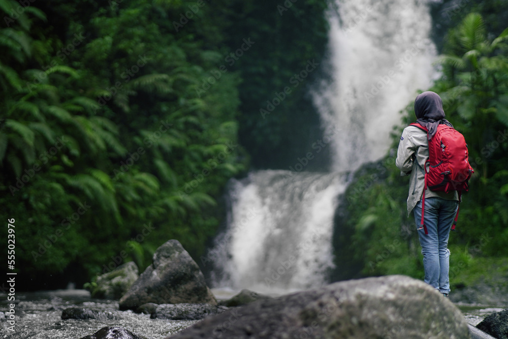 young backpacker women wearing hijab standing backwards and observing the forest and the river young backpacker women wearing hijab standing backwards and observing the forest and the river