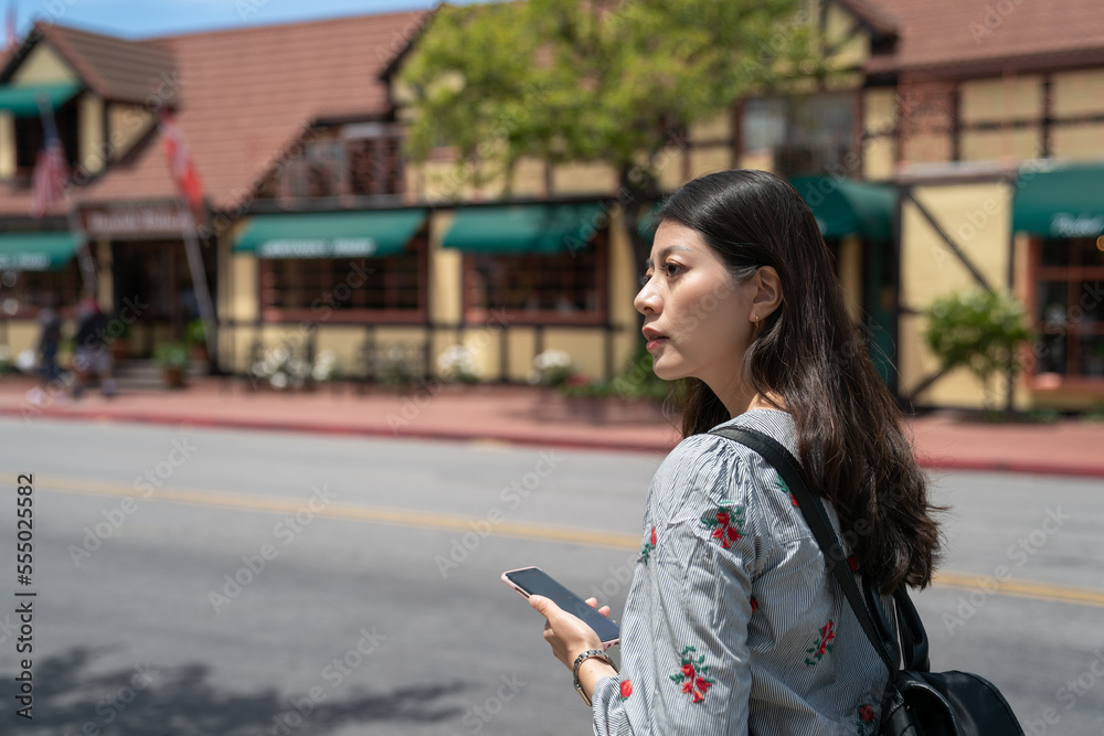 confused asian japanese female traveler looking into space to check directions while using navigation app on the phone on the main street of solvang California usa confused asian japanese female traveler looking into space to check directions while using navigation app on the phone on the main street of solvang California usa