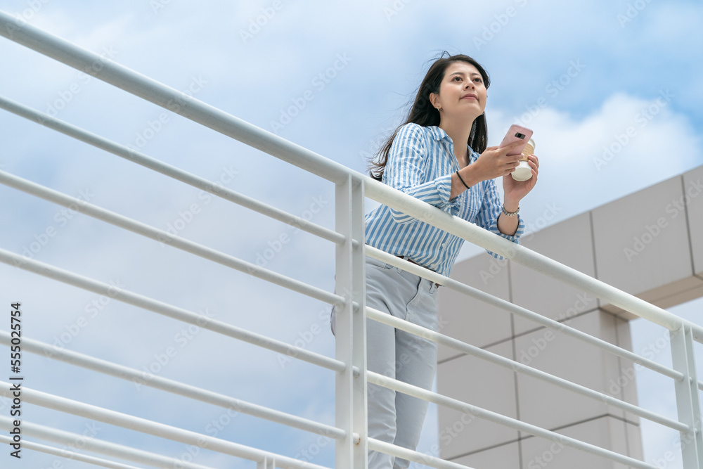 low angle view of leisure asian taiwanese office lady taking coffee break on the edge of deck against blue sky during breaktime at work