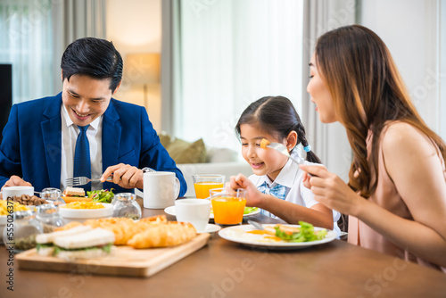 Asian family father  mother with children daughter eating breakfast food on dining table kitchen in mornings together at home before father left for work  happy couple family