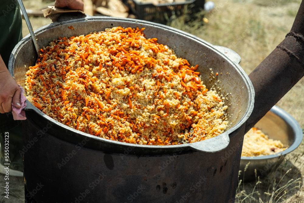 Cooking traditional oriental pilaf in large cauldron on a sunny day outdoor. Real kazakh pilaf