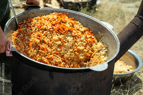 Cooking traditional oriental pilaf in large cauldron on a sunny day outdoor. Real kazakh pilaf in the steppe.