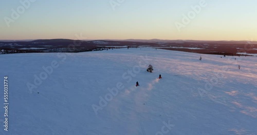 Pair of snowmobile riders speeding across Norbotten, Swedish snow covered landscape at sunrise photo
