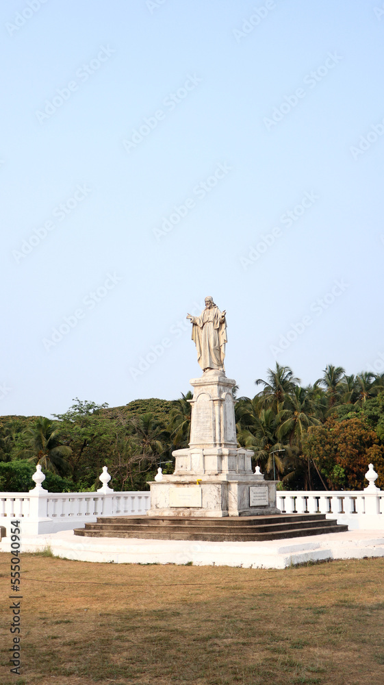 a white statue of jesus christ in the center of a park on a bright summer day