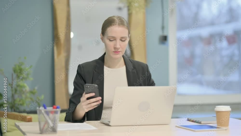 Businesswoman using Smartphone while using Laptop Businesswoman using Smartphone while using Laptop