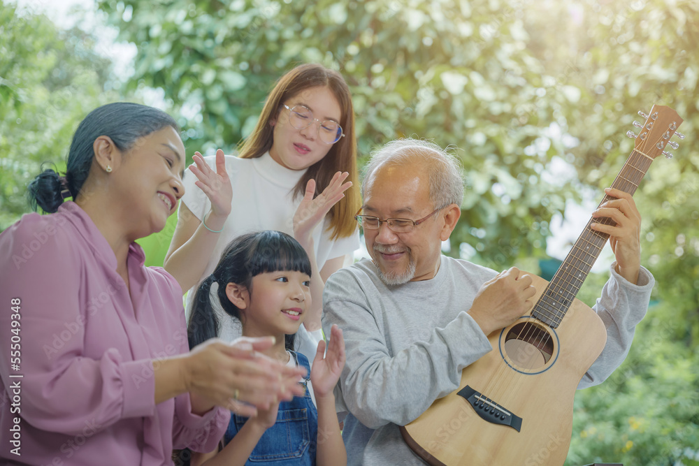Happy family Asian senior elderly man or grandfather playing guitar while his grandmother and granddaughter singing song together outdoors at home, Activity family, Enjoying lifestyle senior older Happy family Asian senior elderly man or grandfather playing guitar while his grandmother and granddaughter singing song together outdoors at home, Activity family, Enjoying lifestyle senior older