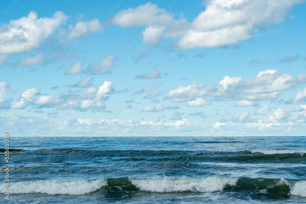 The surface of the sea with a slight wave. Blue sky with clouds over the sea.
