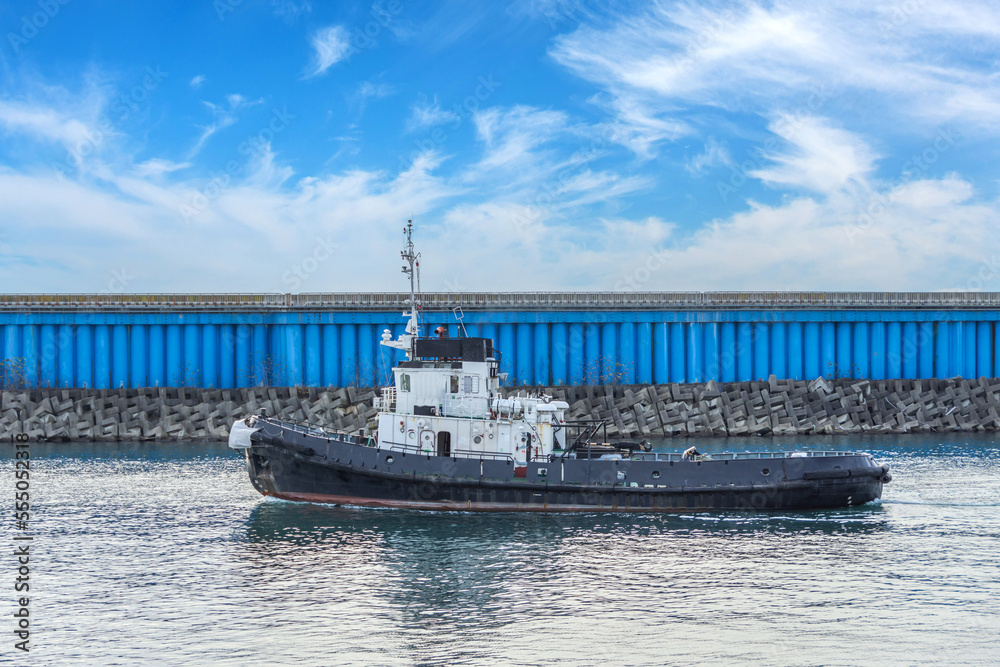 Obraz premium The tugboat passes in the strait of the city port.