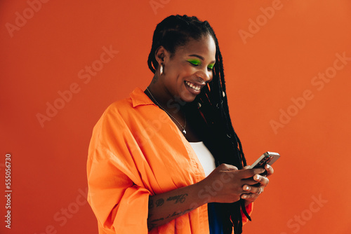 Vibrant, tech-savvy woman with dreadlocks smiles and uses her smartphone to browse the internet in a casual studio setting.